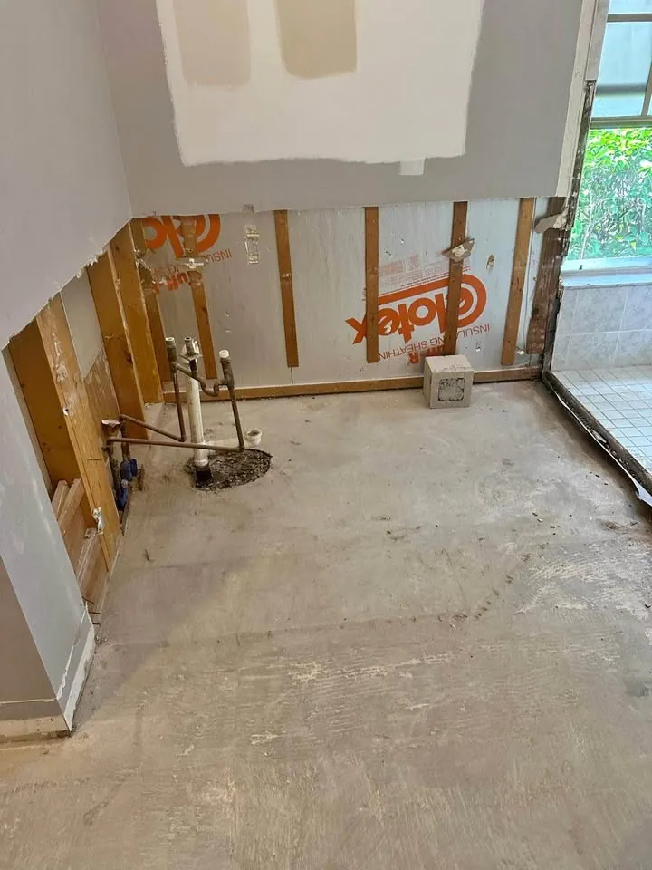 Room with drywall cut away at the base, showing wrapped framing and a bare floor