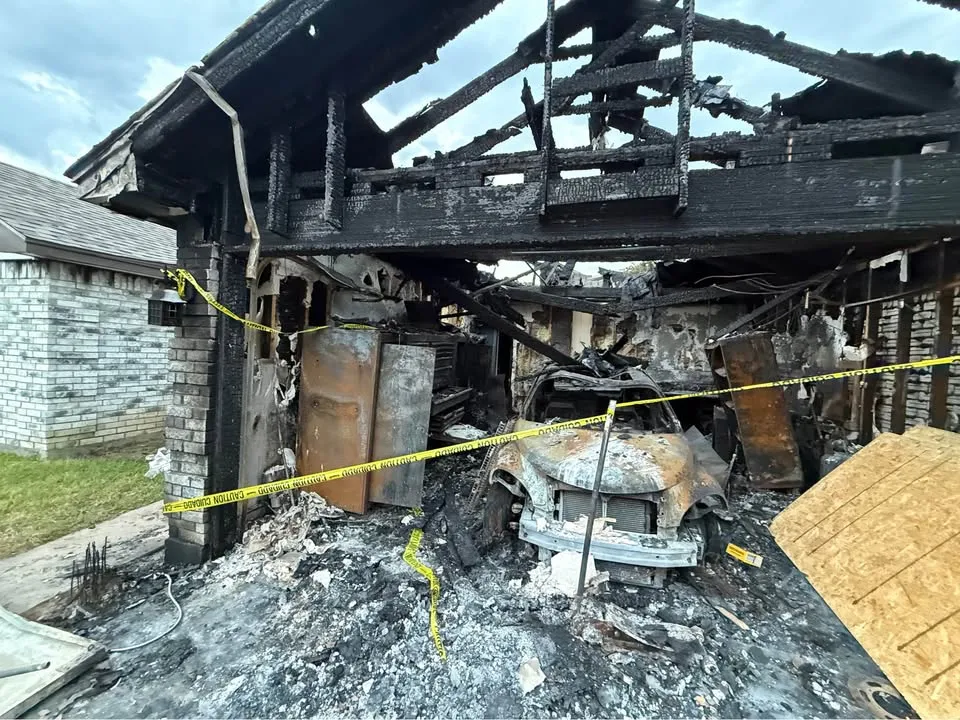 Burned-out garage behind caution tape with charred framing and debris