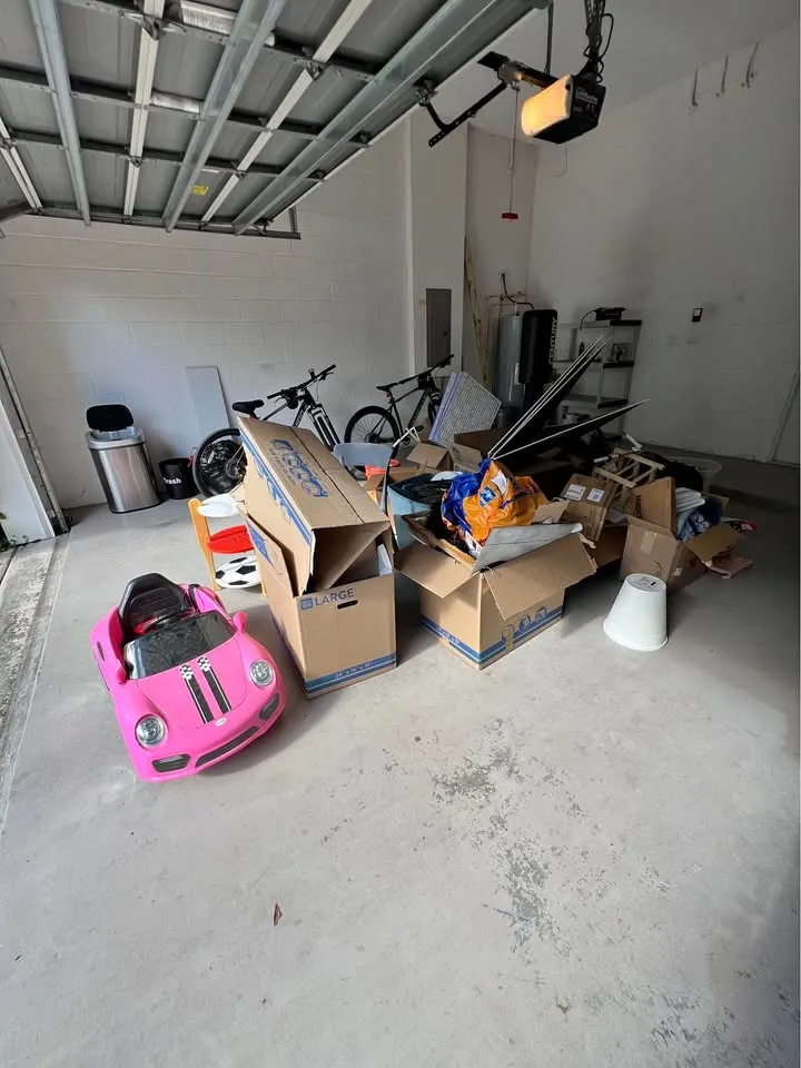 Garage floor loaded with moving boxes, a ride-on toy car and household items ready for removal