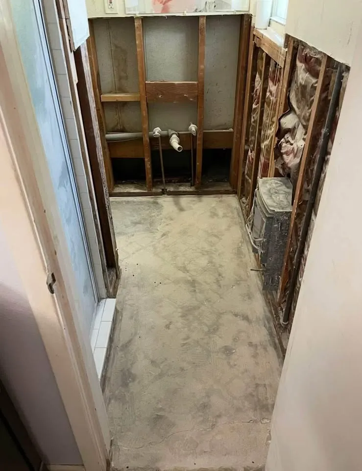 Narrow room with walls stripped to studs and the floor cleared