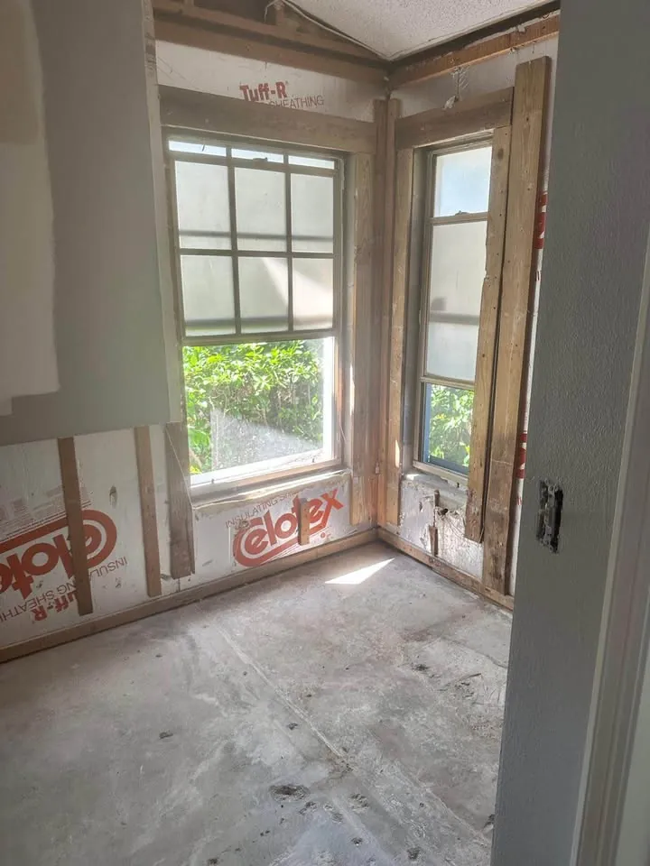 Corner room with lower drywall removed, exposing house wrap and window framing