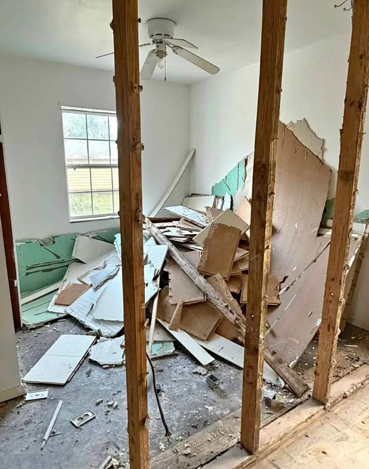 Room with a wall opened between studs and drywall piled behind