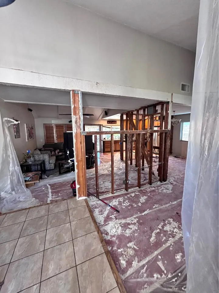 Open-plan room with protective sheeting on the floor and a wall stripped to framing