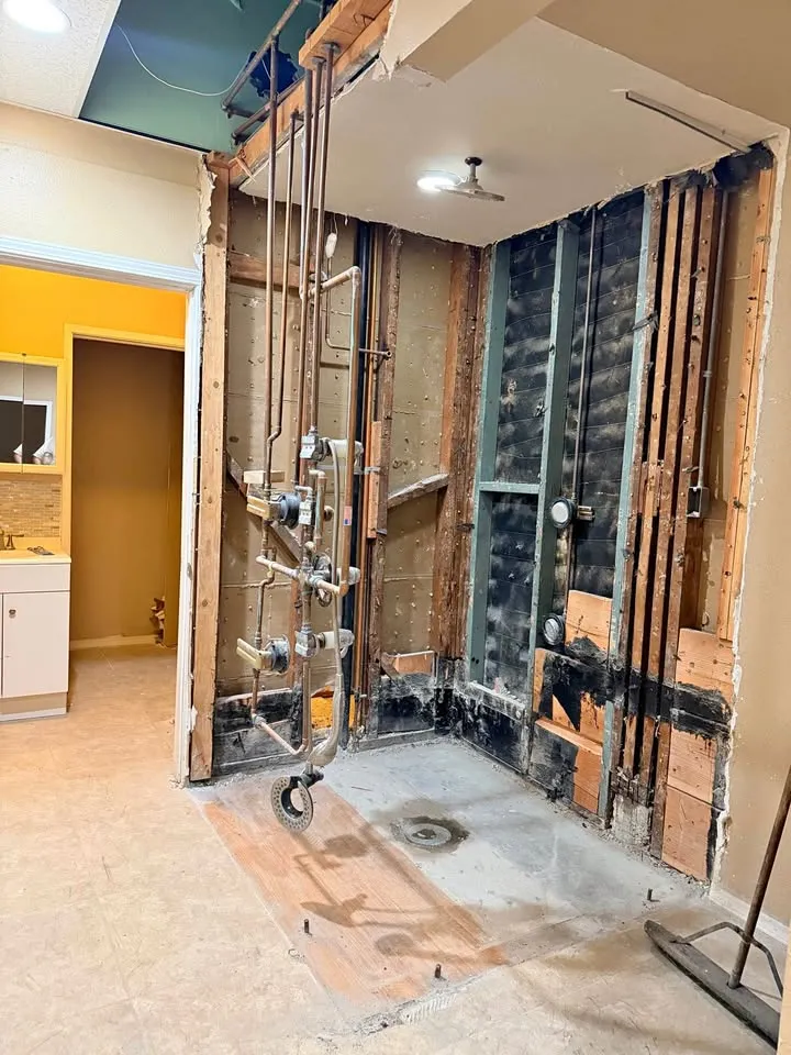 Shower area stripped to the studs with plumbing lines exposed