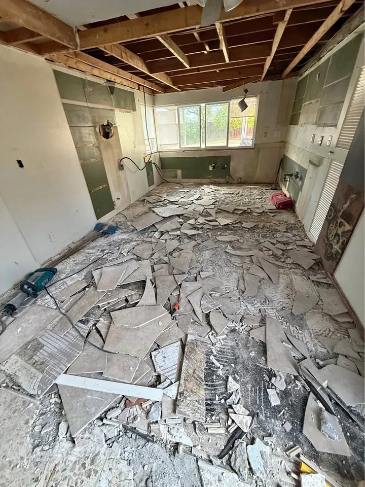 Room with the ceiling opened to joists and broken tile on the floor, materials a pre-demolition asbestos survey samples