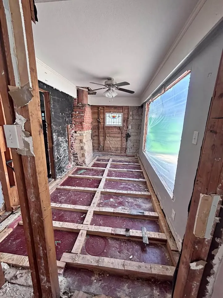 Room with the floor removed down to the joists and a brick wall exposed