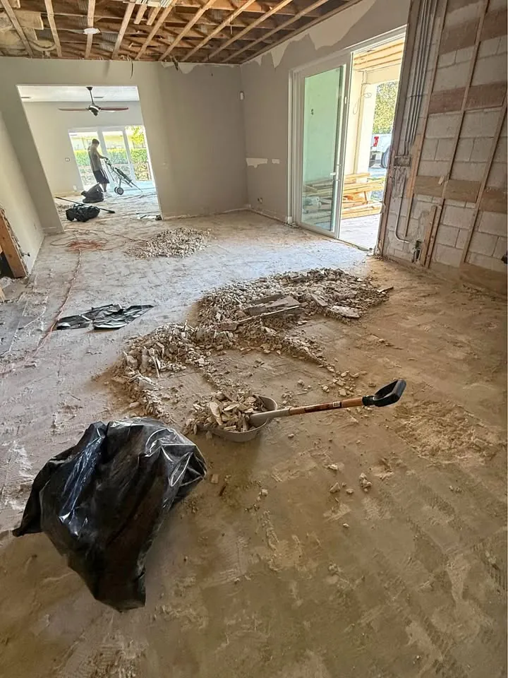 Open-plan space with the ceiling removed and debris and a shovel on the floor