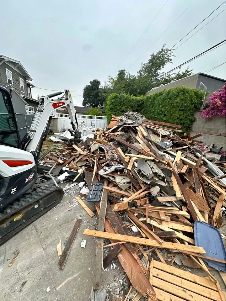 Skid-steer beside a heap of demolished wood framing