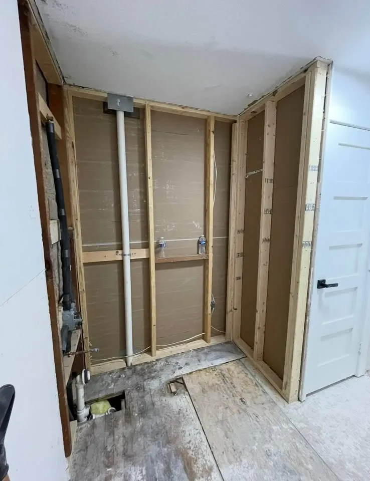Corner with drywall removed, exposing studs and plumbing