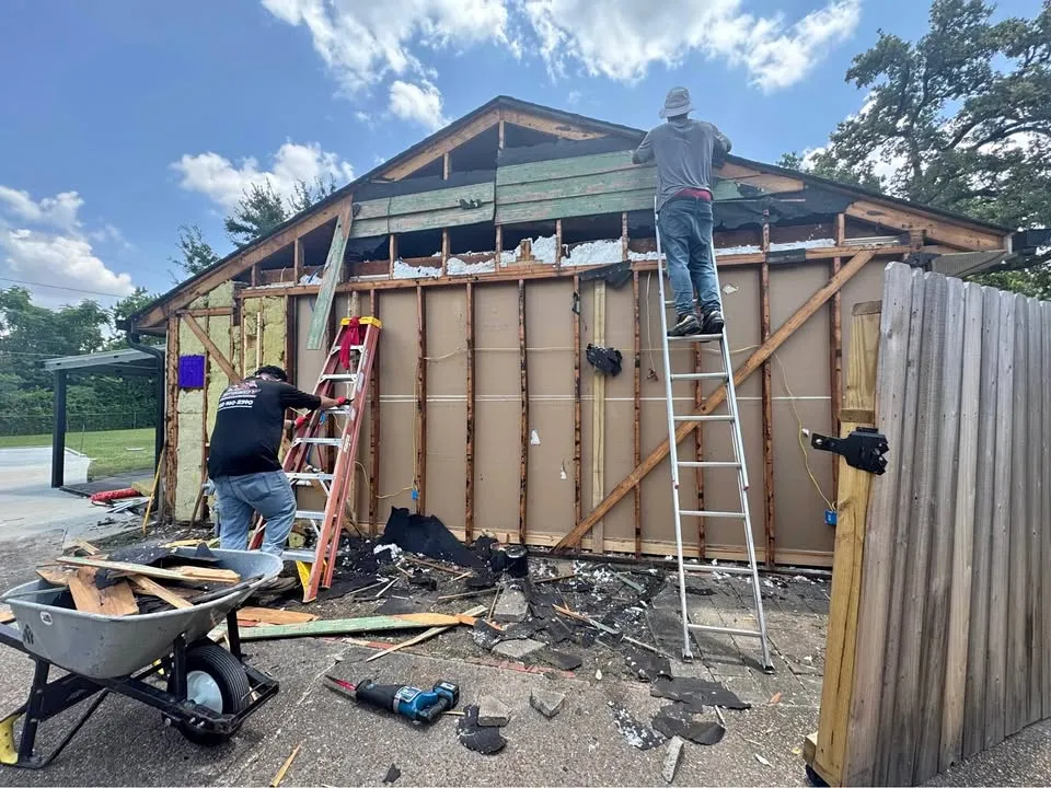 Crew stripping siding and sheathing by hand from a garage before taking down the frame