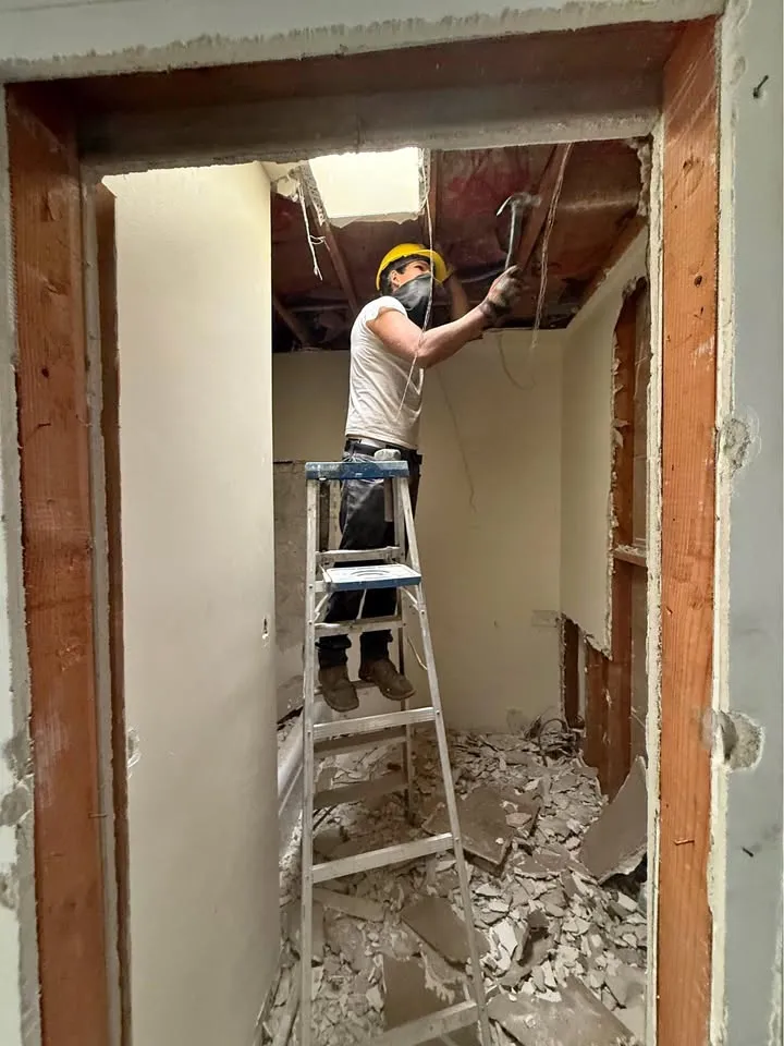 Crew member in a hard hat on a ladder taking down a ceiling during permitted work hours